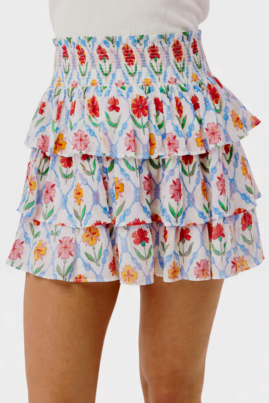 A close-up of the Roller Rabbit Infinity Floral Siggy Skirt, a crinkle chiffon mini with ruffles, featuring red, yellow, pink, and green florals on white. The skirt is styled with a white top.