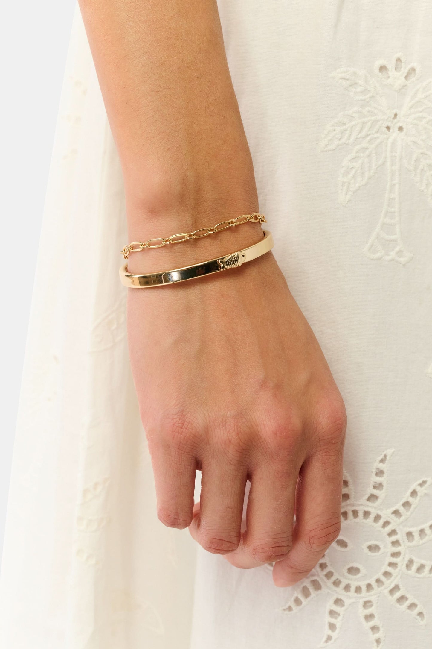 The Roller Rabbit Citra Fish Bracelet Set features a solid open cuff with an engraved detail and a delicate round-link chain with clasp, both shown on white. This elegant gold set is versatile for any occasion.