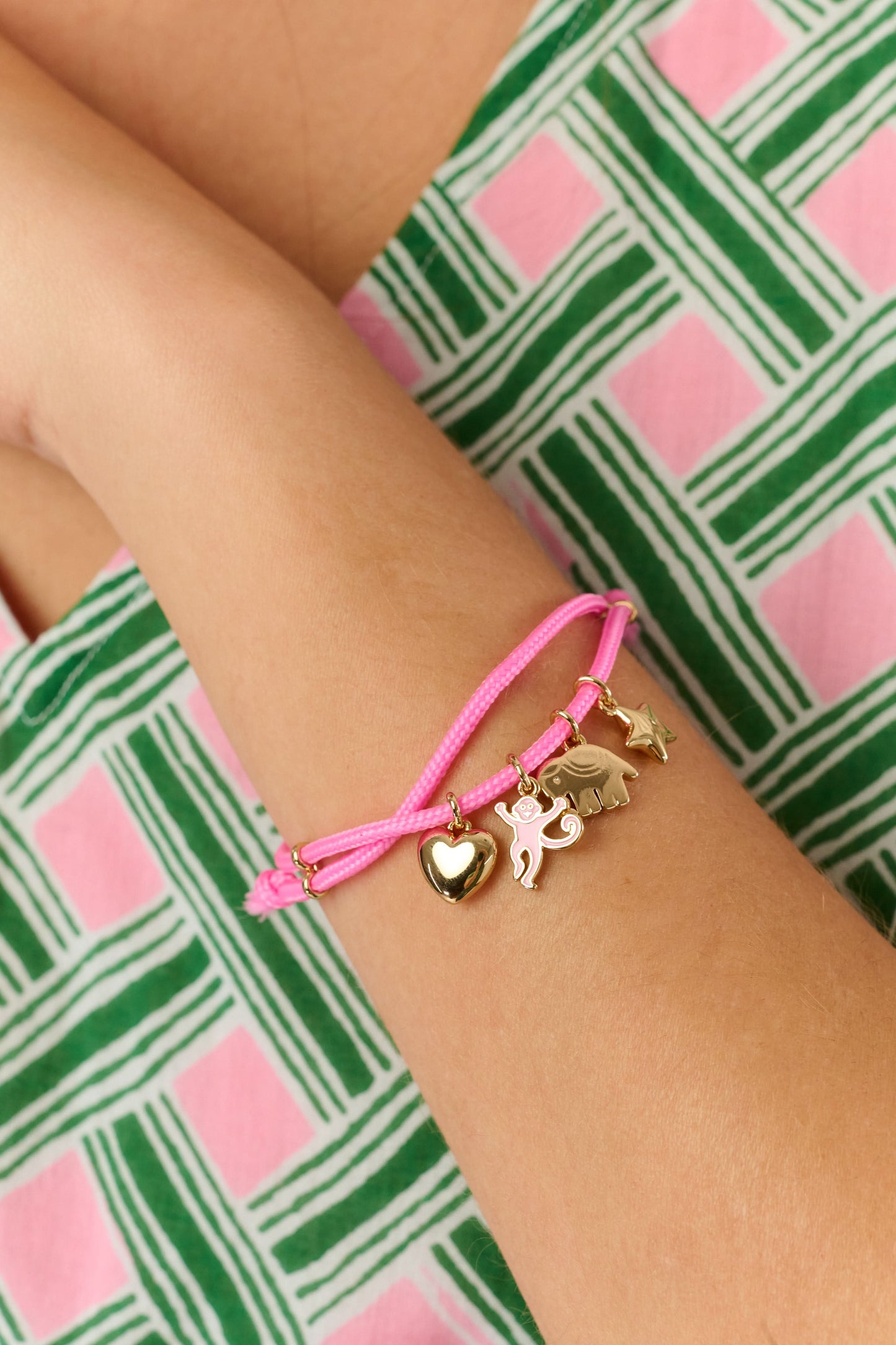The Roller Rabbit Icon Party Charm Bracelet is a pink adjustable bracelet with five gold-tone charms—a heart, unicorn, butterfly, cat, and star—shown on a plain white background.
