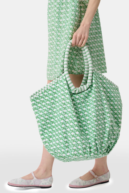 The Cane Bondi Bag by Roller Rabbit is a green and white tote with a wide, round handle, side ties, and a repeating fish pattern on soft cotton canvas. Its unique flared shape adds style to this charming everyday bag.