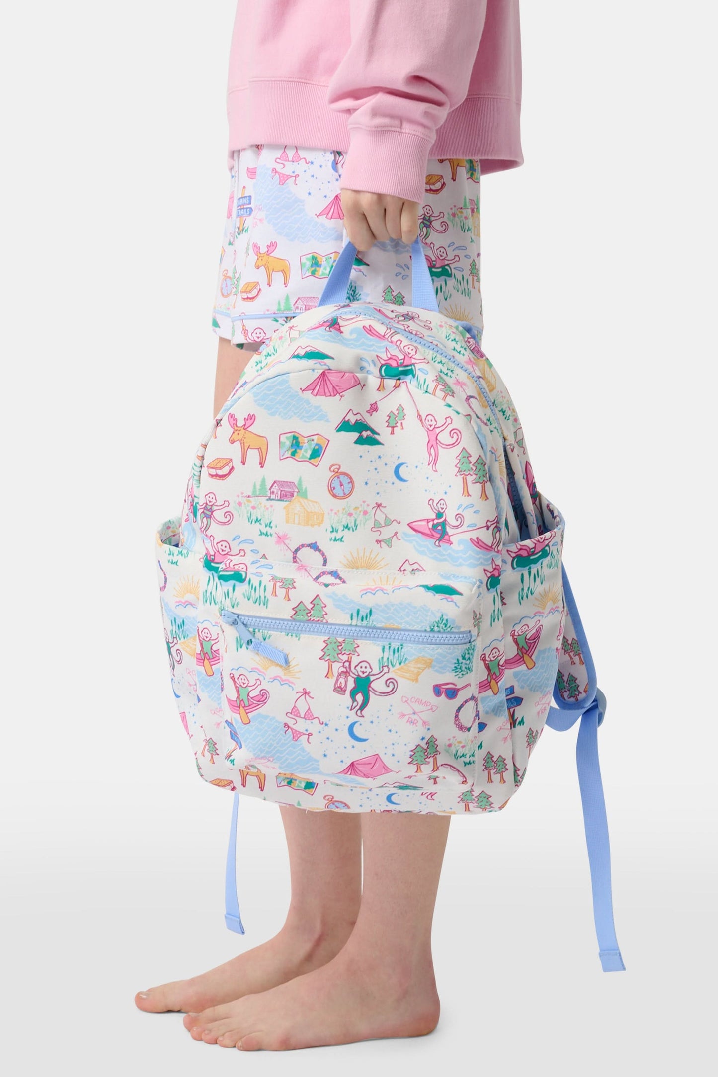 The Camp RR Backpack by Roller Rabbit features colorful cartoon camping scenes—mountains, animals, tents, trees, and rivers—plus playful characters in pink, blue, yellow, and green.