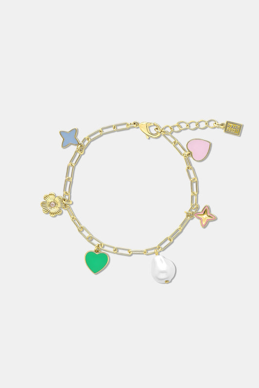A person in a dark blue, eyelet-patterned top crosses their arms, showcasing the Roller Rabbit Celine Heart Bracelet adorned with candy-colored charms like a green heart, flower, and pearl.