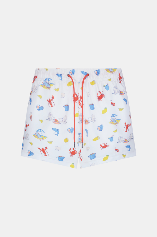 A person stands barefoot, one hand in a pocket, wearing a white T-shirt and Roller Rabbit Men's Catch of the Day Swim Trunk with colorful beach-themed prints, an elastic waistband, and a classic fit.