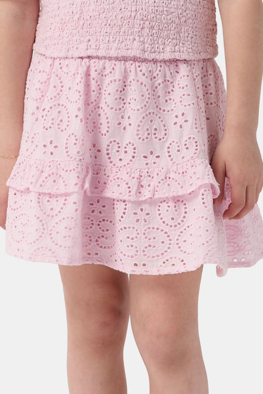 A young child wears the Roller Rabbit Kids Clover Eyelet Emry Skirt in light pink with ruffles and a matching smocked top, standing with their left arm slightly bent against a plain white background.
