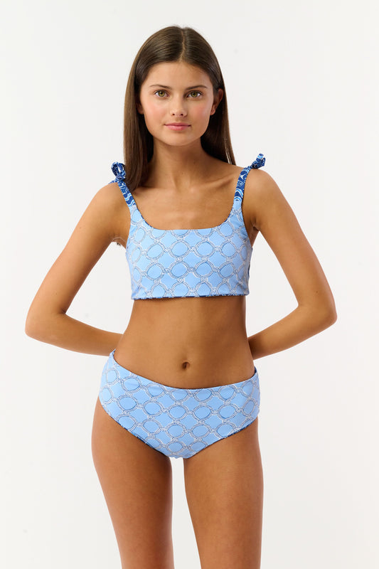 A girl in the Roller Rabbit Kids Fish Stripe/Ruban Reversible Cora Bikini stands by a pool, holding a striped towel behind her with outstretched arms. Her long hair is loose, and her swimwear offers UPF 50+ sun protection. Face partially out of frame.