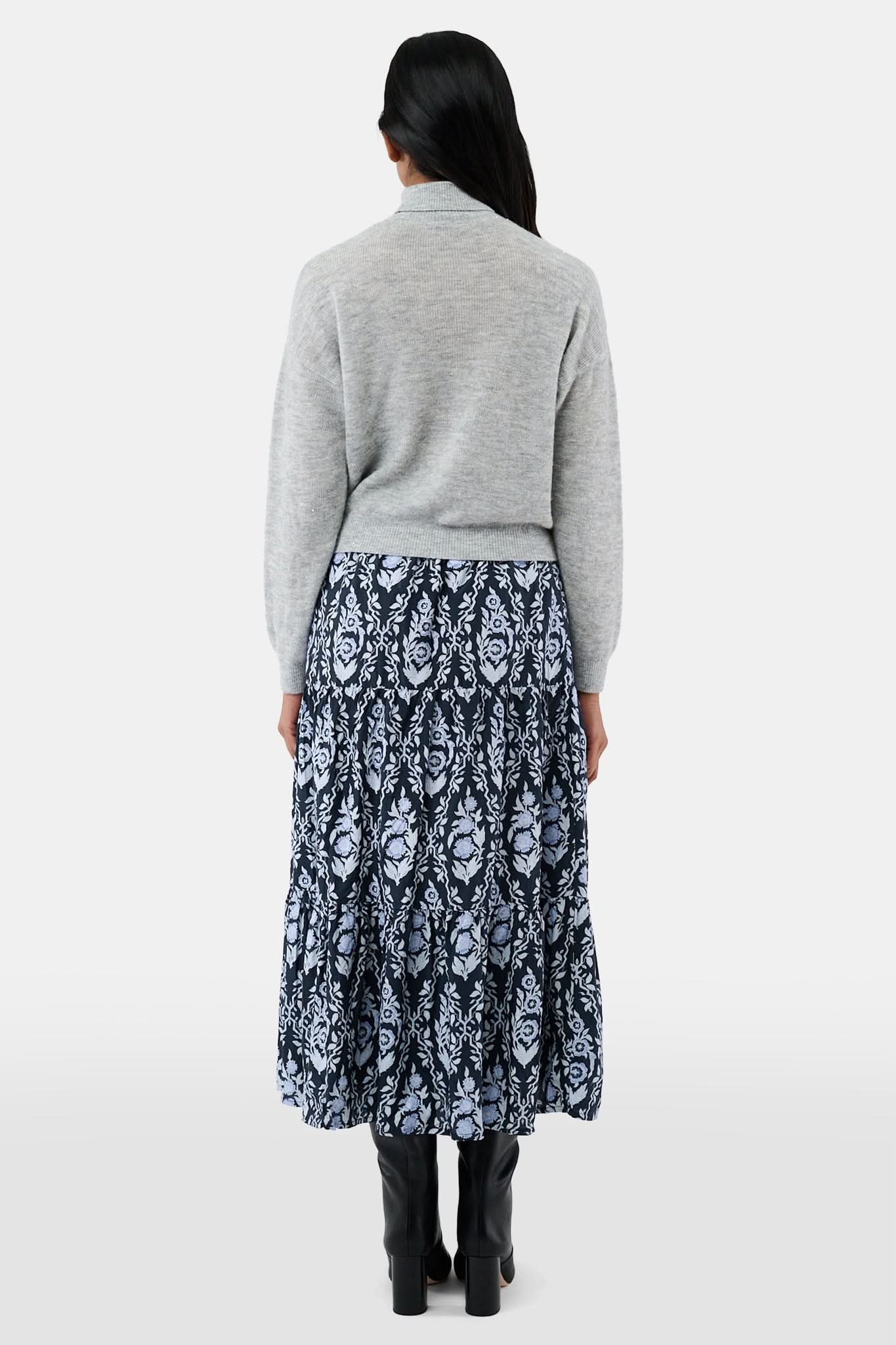A woman with long dark hair is wearing the Roller Rabbit Heather Sequins Felice Sweater and a navy blue skirt with a white floral pattern, standing against a plain white background.