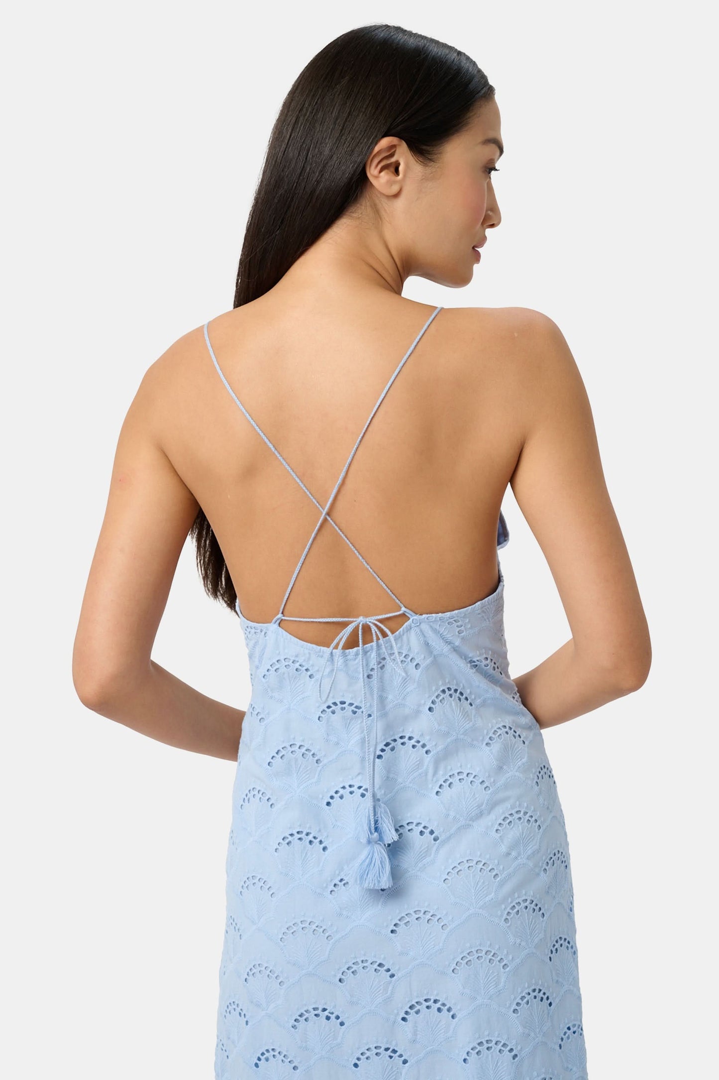 A woman wears the Roller Rabbit Jemina Eyelet Athena Dress, a sky blue, sleeveless cotton sundress with a gathered halter neckline and eyelet details, paired with white sandals, set against a plain white background.