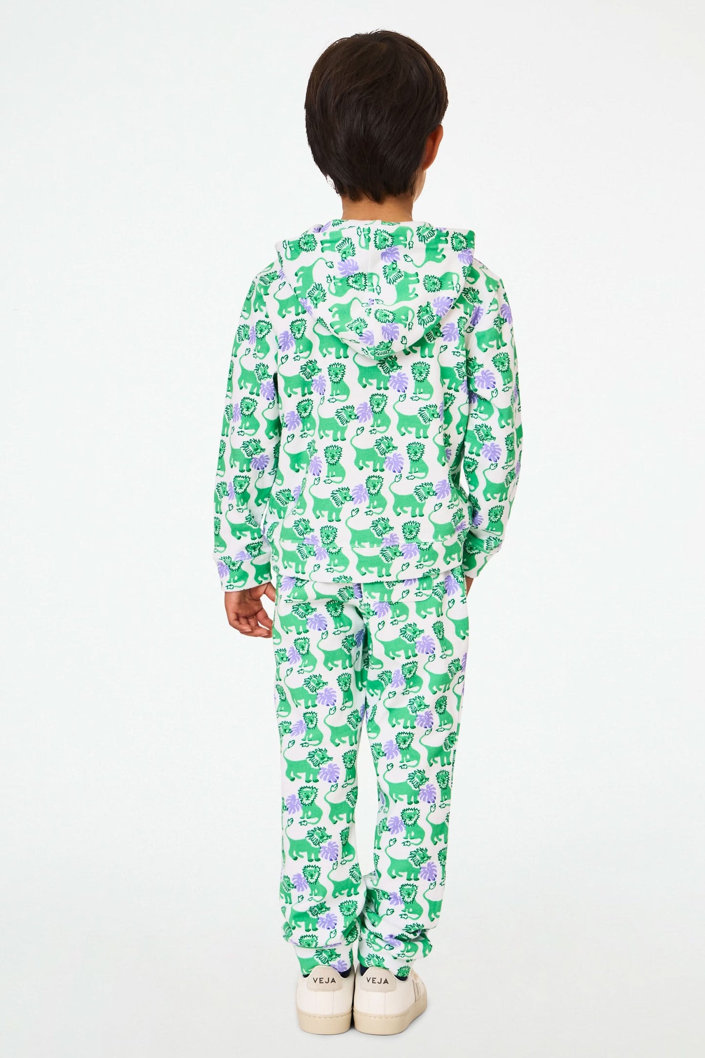 A young child wears the Roller Rabbit Kids Leo The Lion Harley Hoodie, a green and purple French terry zip-up with matching pants, featuring a Leo the Lion print, posing with hands in pockets against a plain white background.