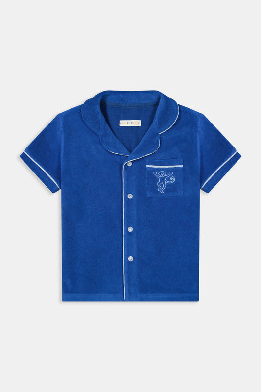 A young child wearing the Roller Rabbit Kids Monkey Embroidery Leo Polo—a navy top with white trim and an embroidered monkey on the chest pocket—smiles with arms raised overhead.