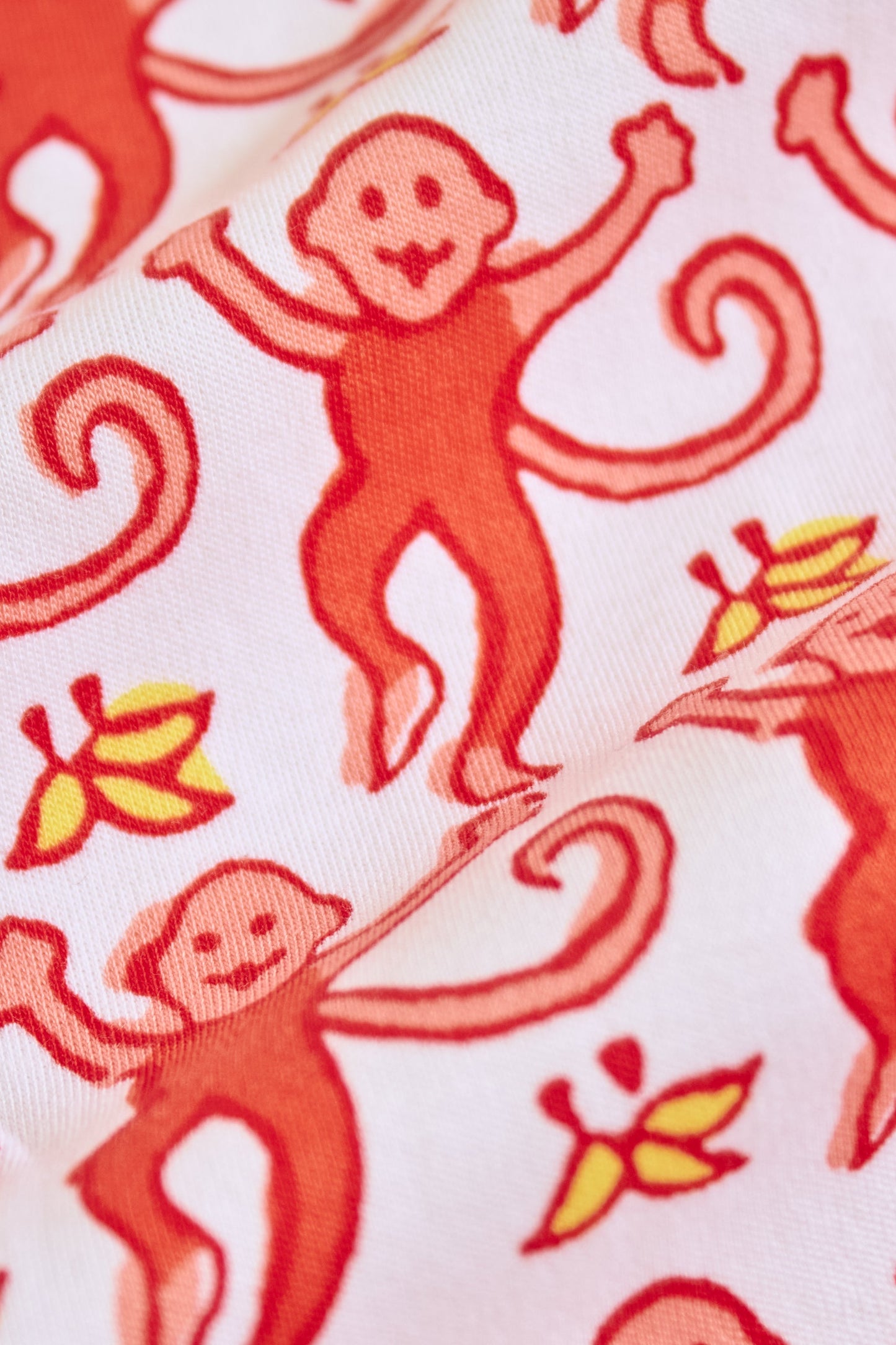 Close-up of Monkey Polo Pajamas: playful red monkey pattern with smiling faces and curled tails, plus yellow and orange leaves on a light pink background—perfect for matching pajama sets in soft pima cotton.