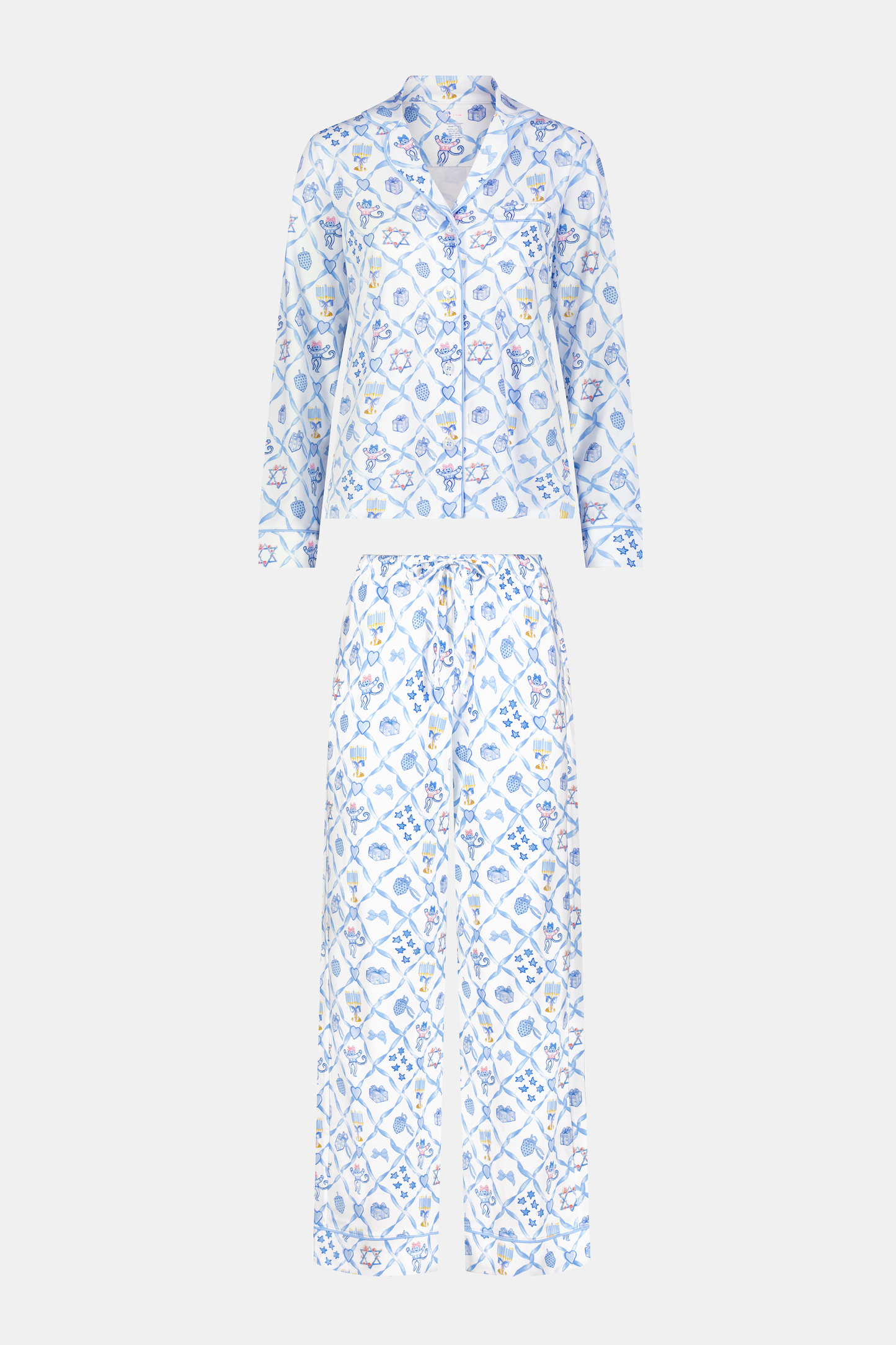A woman smiles barefoot on a white background, hands in pockets, wearing Roller Rabbit's Starry Nights Lattice Long Sleeve Polo Pajamas—cozy loungewear crafted from soft Pima cotton.