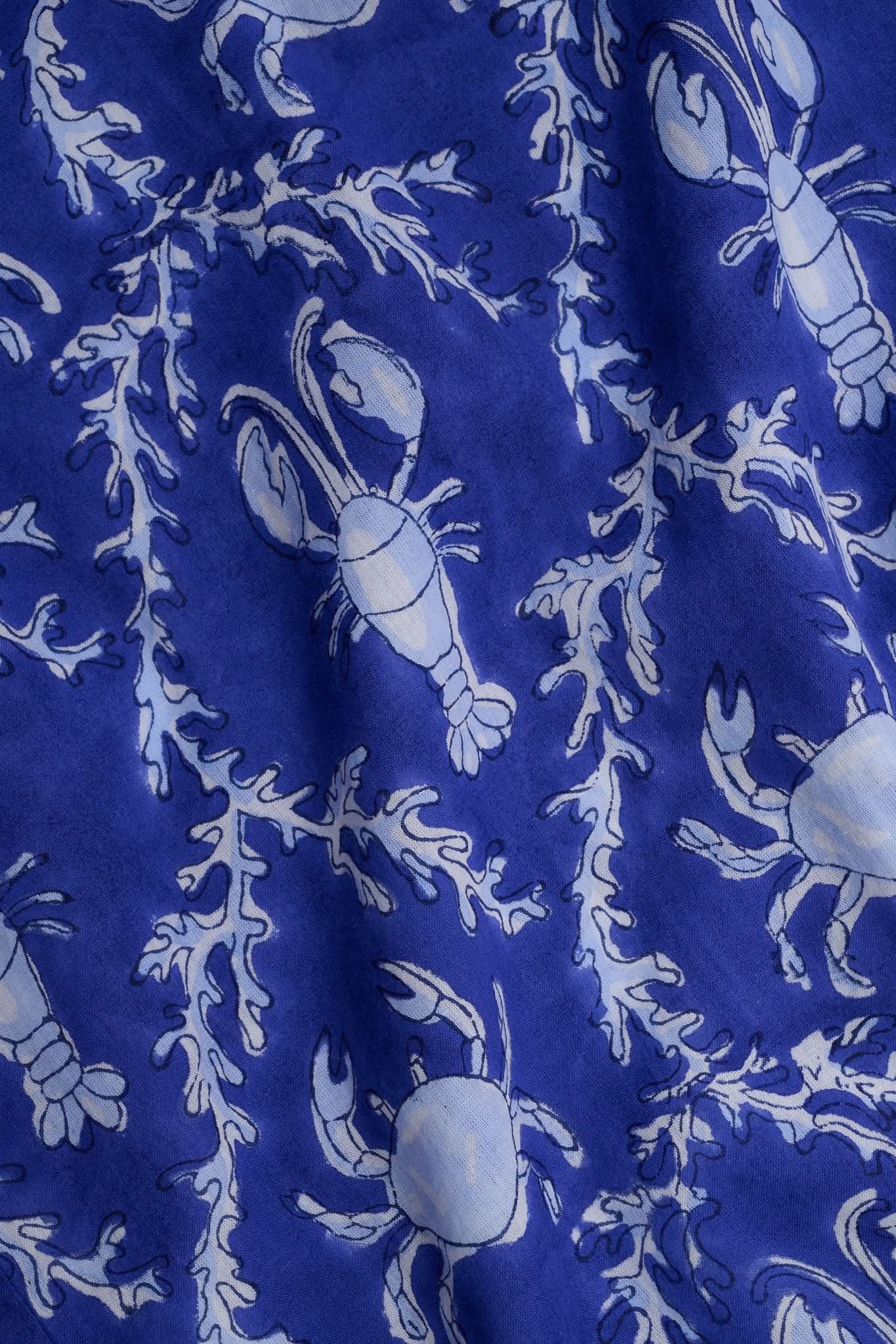 A woman wears the Roller Rabbit Lobster Trellis Johanna Caftan in blue and white, featuring a white V-neckline and hem, paired with sandals against a plain background.