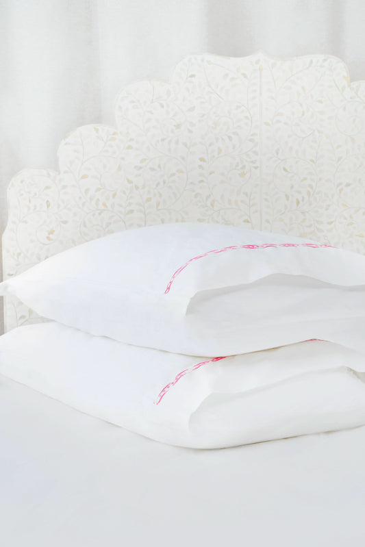 Two white Francis Embroidered Pillowcases by Roller Rabbit, made of 100 cotton with a 300 thread count, are arranged on a matching bed. A scalloped, floral headboard provides an elegant backdrop.
