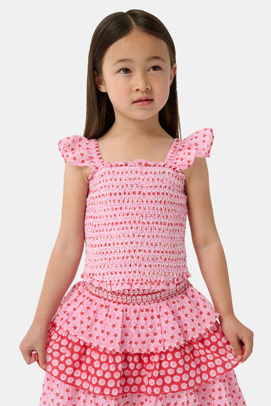 A young girl wears the Roller Rabbit Kids Starry Dot Tory Top in pastel pink with flutter sleeves, paired with a matching skirt featuring red stars and white polka dots. Only her torso and part of her face are visible.