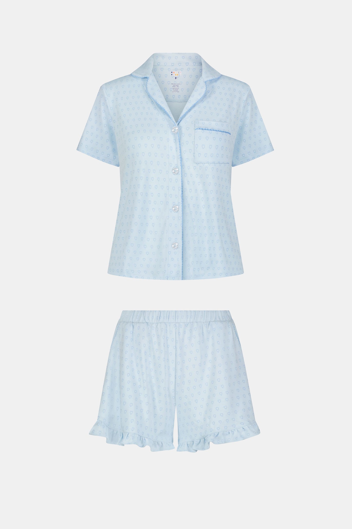 A woman wears Roller Rabbit's Hearts Tonal Wyatt Polo Pajamas—light blue, short-sleeved Pima cotton with a collar and chest pocket—paired with matching ruffled shorts, standing against a plain light background.