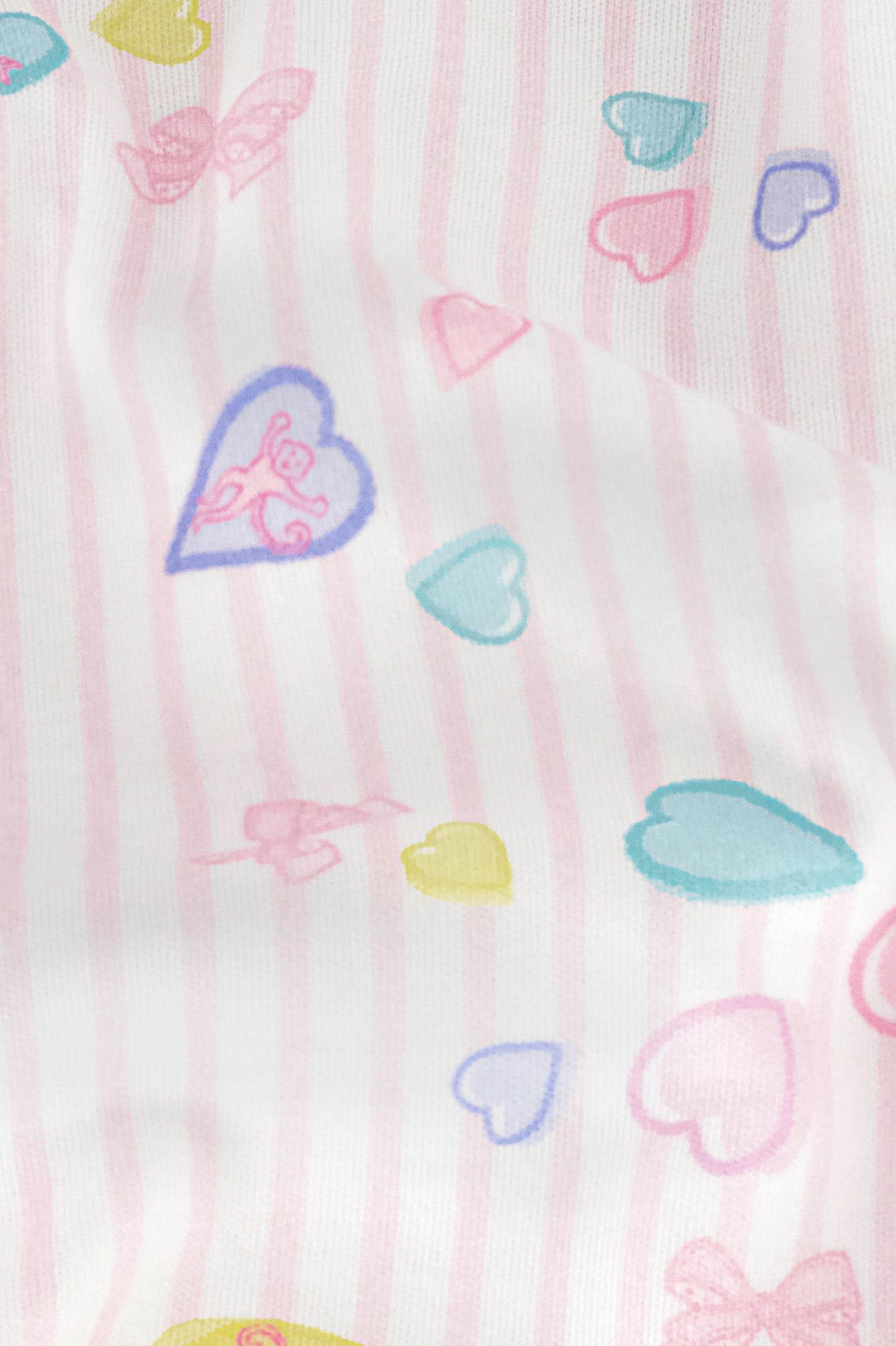 Wearing Roller Rabbit's Candy Heart Stripe Jones Shortie pajama shorts, featuring a pastel hearts, bows, and stars pattern, this person stands against a light background.