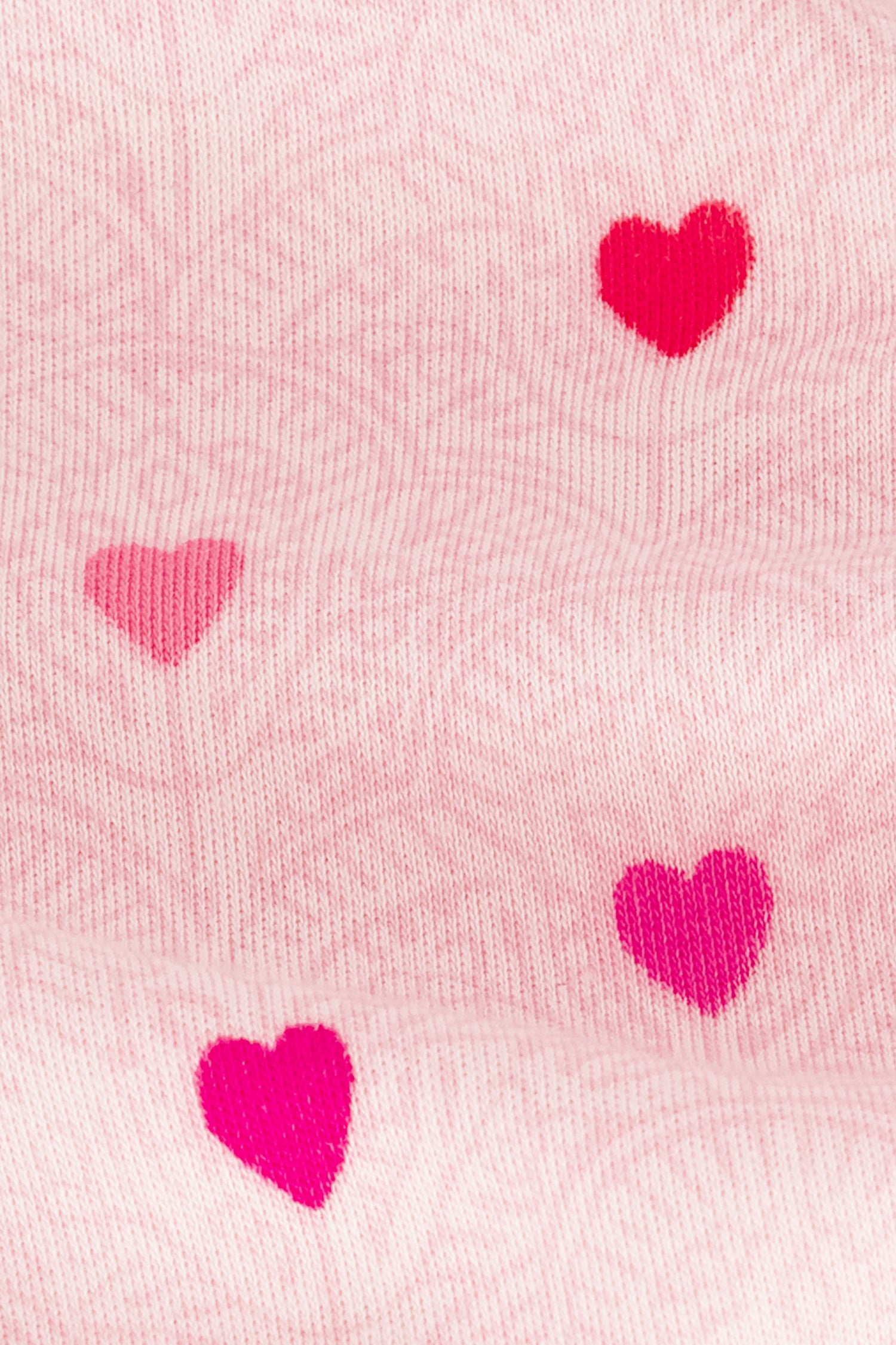 A close-up of blush pink ribbed fabric from the Jemina Hearts Kate Set by Roller Rabbit shows five red and pink hearts in its signature Jemina Hearts print.