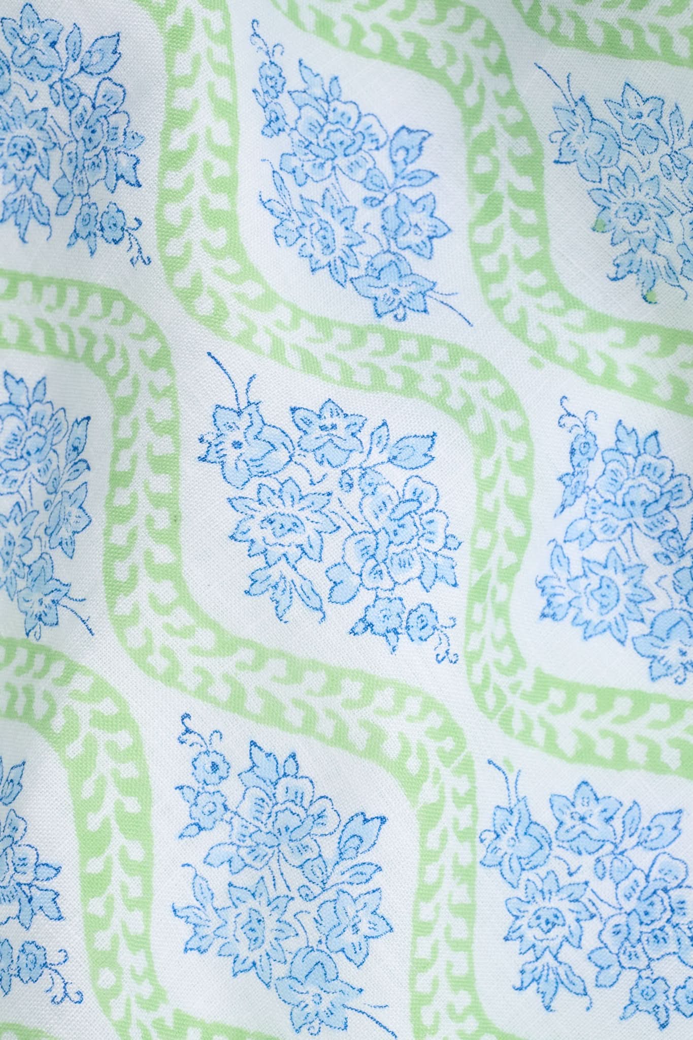 A woman faces forward in the Roller Rabbit Zelda Floral Shiv Caftan, a loose, ankle-length dress with a blue and green geometric print. She has long dark hair, white sandals, and stands against a plain white background.
