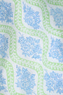 A woman faces forward in the Roller Rabbit Zelda Floral Shiv Caftan, a loose, ankle-length dress with a blue and green geometric print. She has long dark hair, white sandals, and stands against a plain white background.