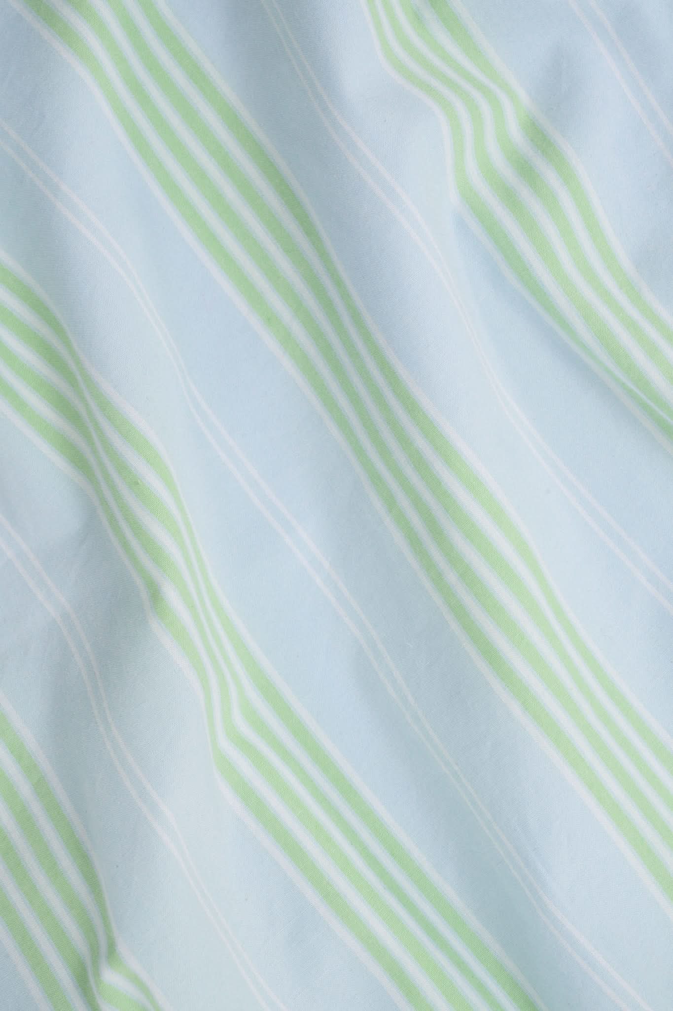 A woman with long brown hair wears the Roller Rabbit Positano Stripe Cooper Set, featuring a loose, sleeveless cotton poplin top with ruffle trim and drawstring, and elastic-waist shorts in white fabric with light green vertical stripes.