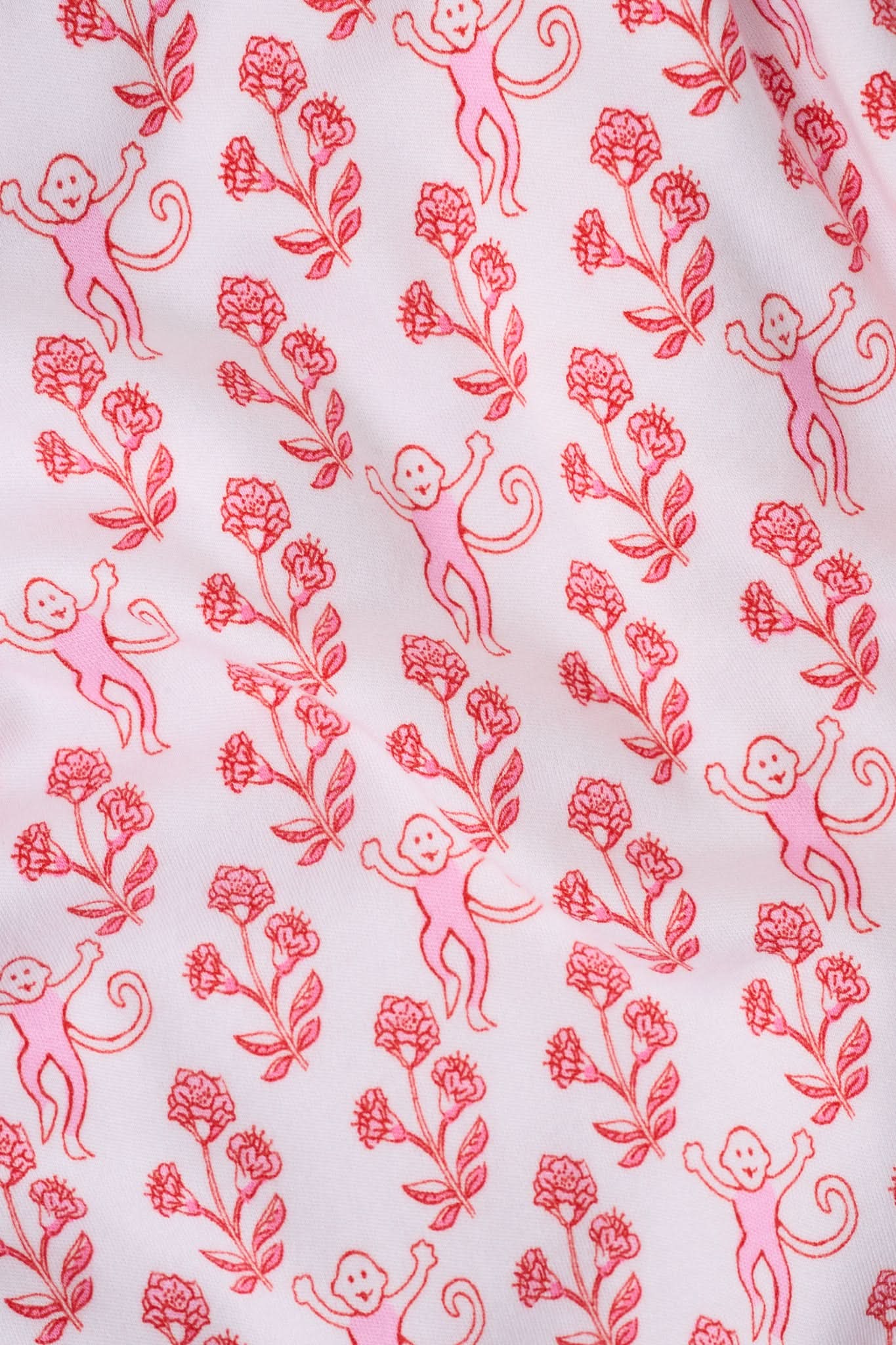 Wearing the Roller Rabbit Rosa Ditsy Monkey Hayden Pajamas—a pink and white set with a small anchor print, long-sleeve button-up top, and ruffled shorts—a person stands against a plain light background, smiling slightly.