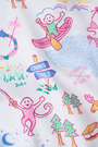 A woman with long brown hair wears the Roller Rabbit Camp RR Mischa Set, a light-hued Pima cotton pajama set with playful prints. The adjustable strap tank and shorts provide comfort as she stands turned slightly to the side, gazing off-camera.