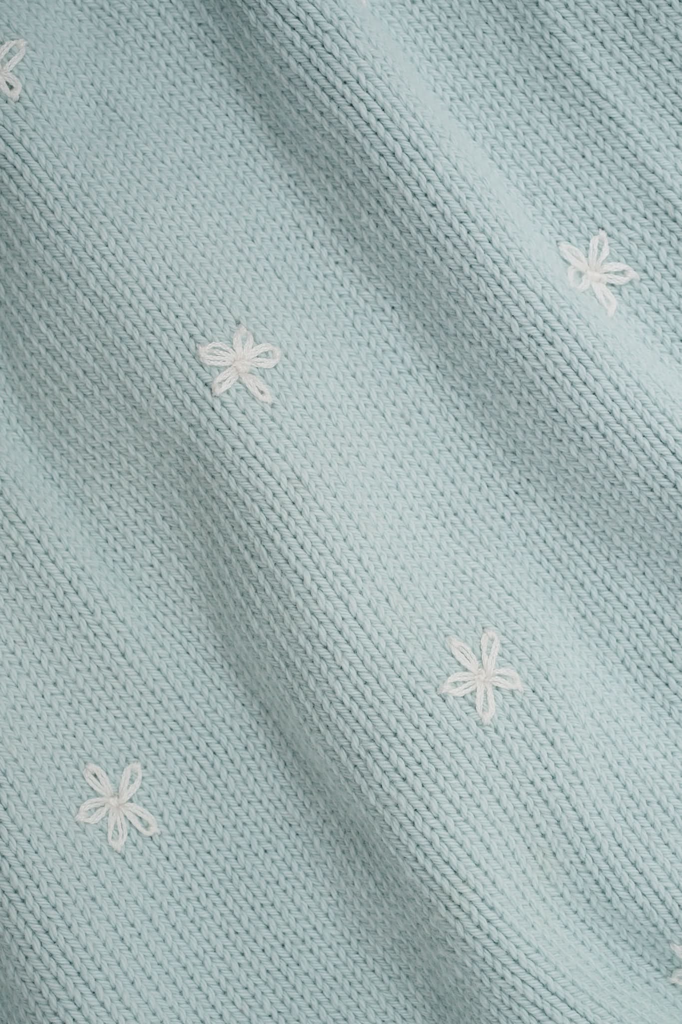 Close-up of a woman wearing the Roller Rabbit Floral Bloom Nyla Cardigan, a light blue cotton button-up with white embroidered stars, rounded neckline, and short sleeves, styled with white eyelet shorts.