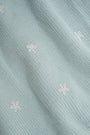 Close-up of a woman wearing the Roller Rabbit Floral Bloom Nyla Cardigan, a light blue cotton button-up with white embroidered stars, rounded neckline, and short sleeves, styled with white eyelet shorts.