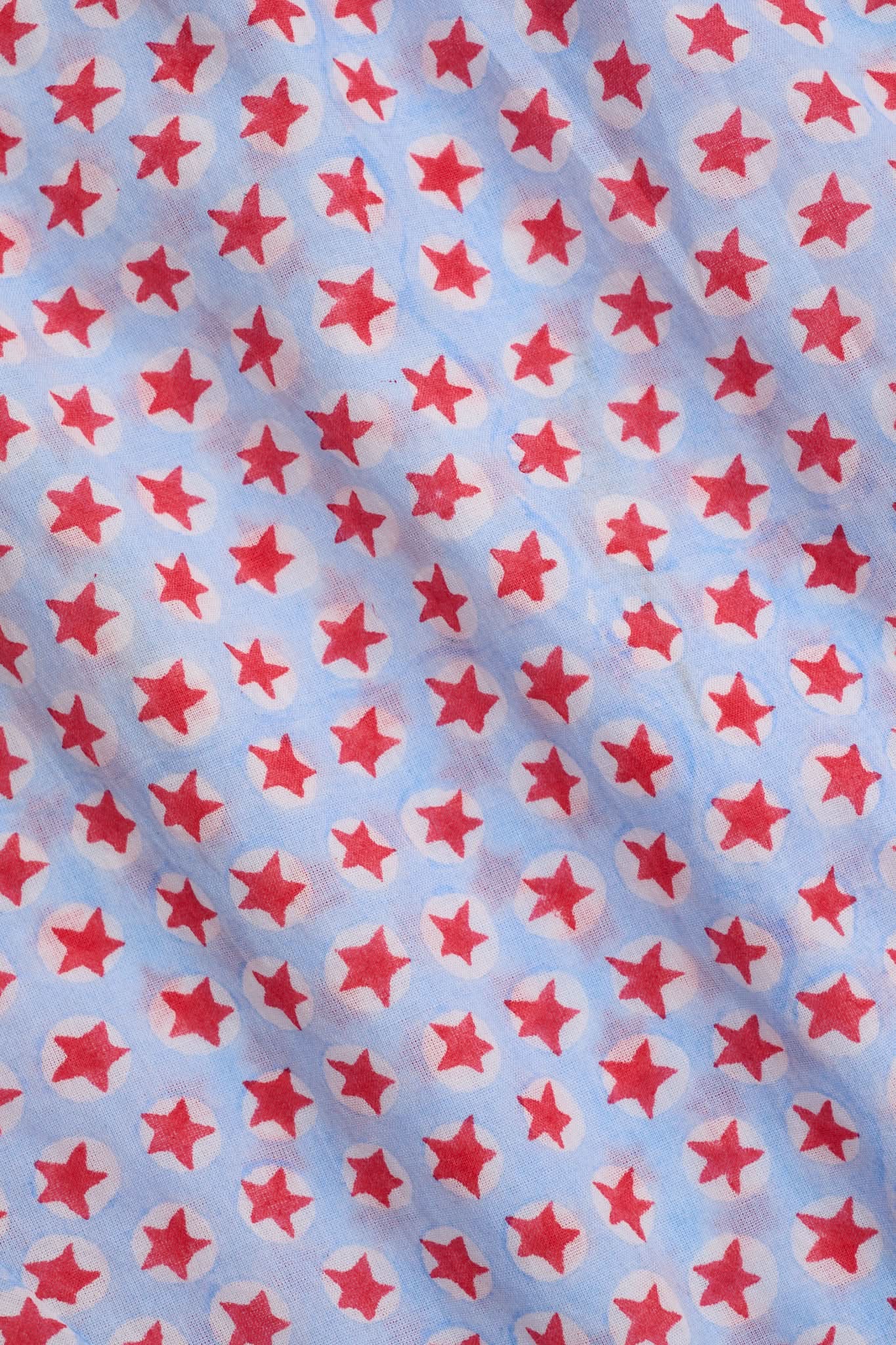 A young girl with long brown hair stands facing forward in the Roller Rabbit Kids Starry Dot Carrie Cover Up—a sleeveless, knee-length white dress featuring a red dotted pattern and pom-pom trim. She has a neutral expression and a light background behind her.