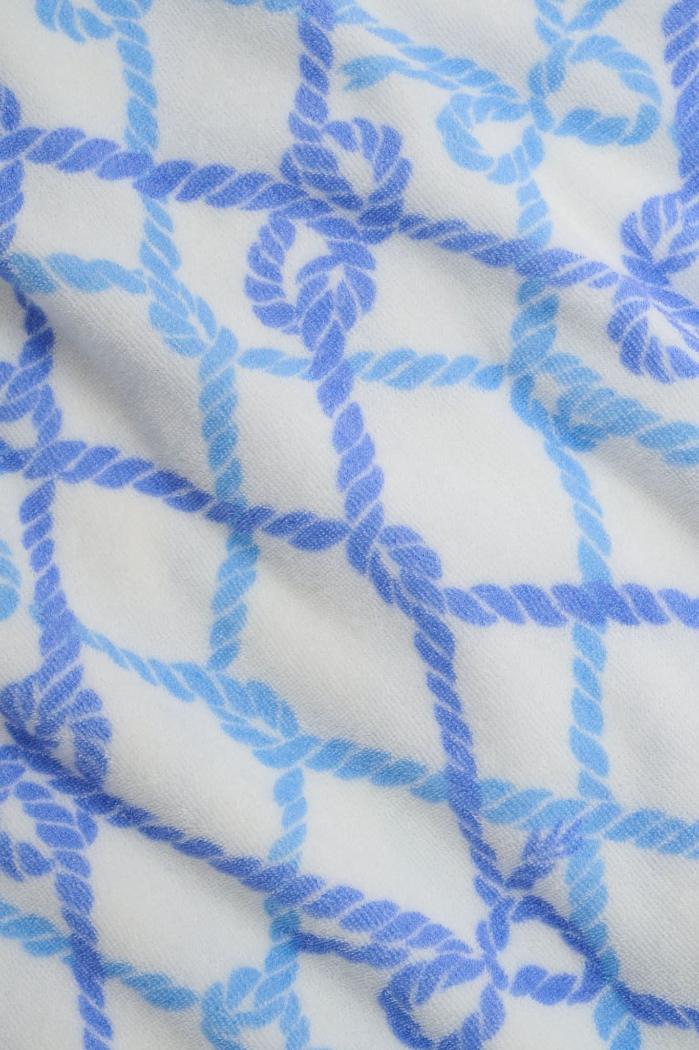 A person wears the Roller Rabbit Seaside Knots Mara Pant, featuring a tie waist and wide legs in loose white fabric with a light blue geometric chain pattern, paired with a matching top and white sandals against a plain white background.
