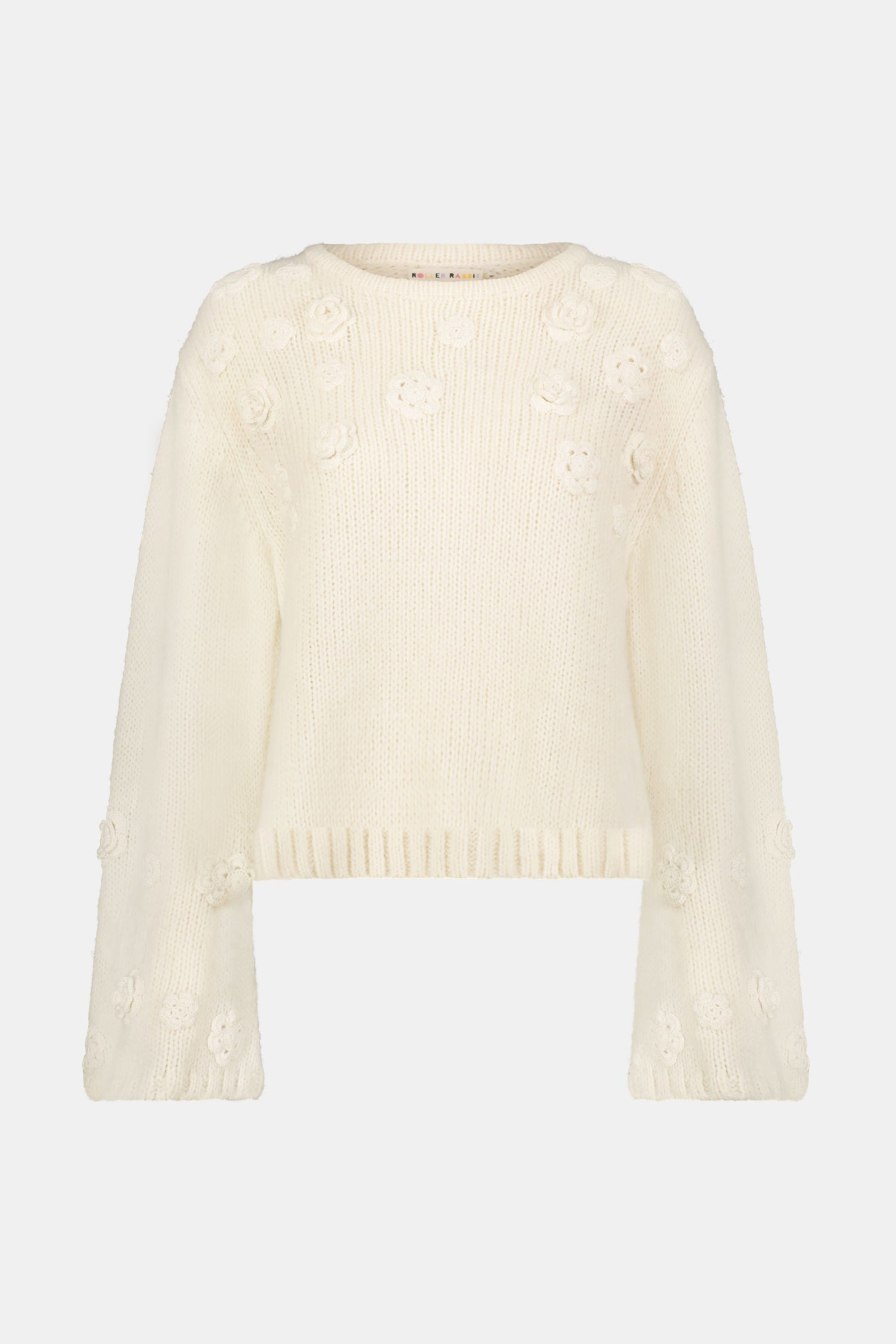 The Crochet Floral Quinn Sweater is a cream, long-sleeve knit with a crew neck and delicate crochet floral accents on the sleeves and chest, made from an alpaca wool blend and shown against a white background.