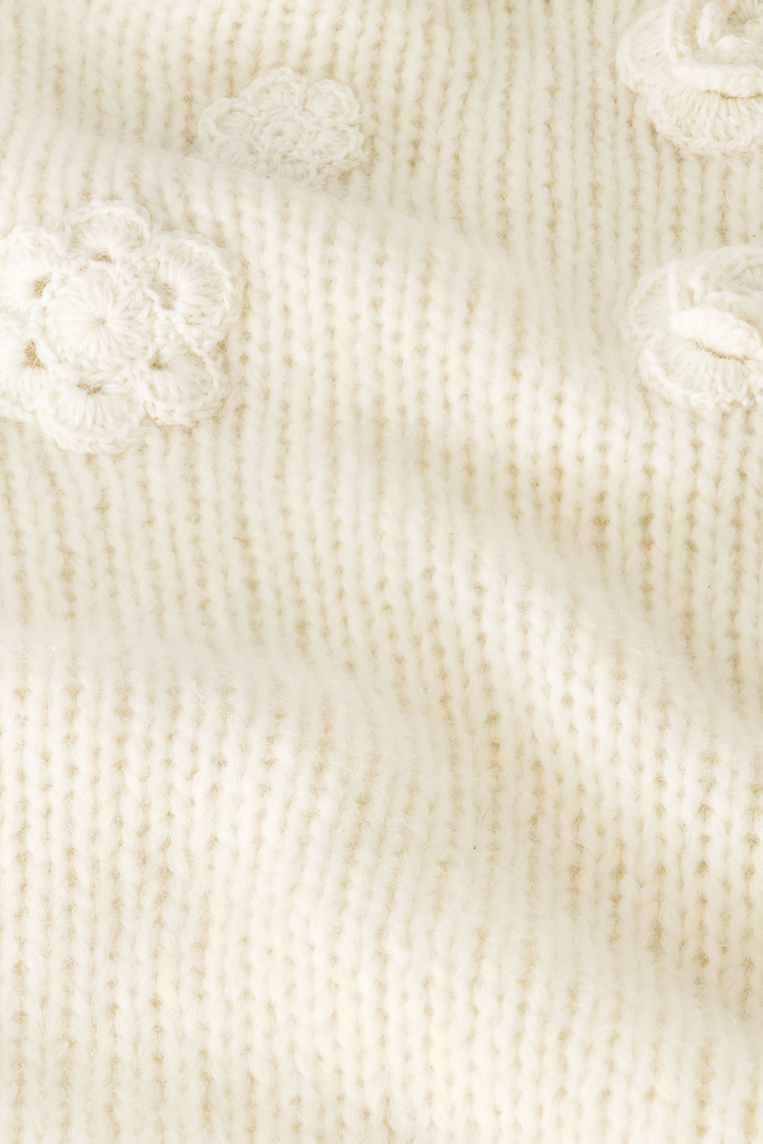 A close-up of the Crochet Floral Quinn Sweater’s soft, cream knit showcases raised crochet floral details and textured stitches, giving it a cozy, delicate look.