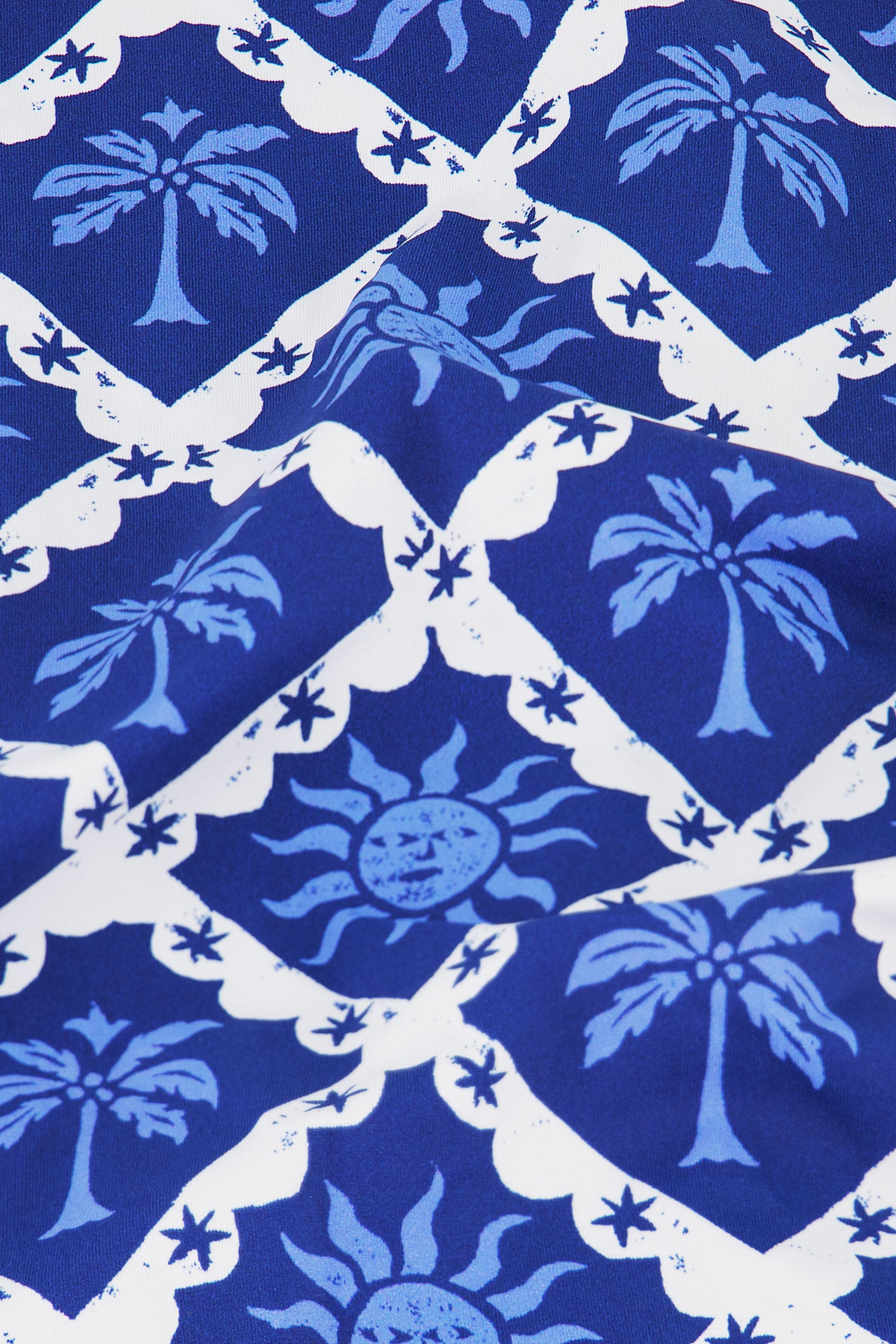 A person wears the Roller Rabbit Sunny Days Serena Bikini Bottom, featuring adjustable hip ties and a blue and white palm tree and abstract sun print with medium coverage, set against a plain white background.