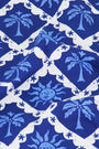 A person wears the Roller Rabbit Sunny Days Serena Bikini Bottom, featuring adjustable hip ties and a blue and white palm tree and abstract sun print with medium coverage, set against a plain white background.