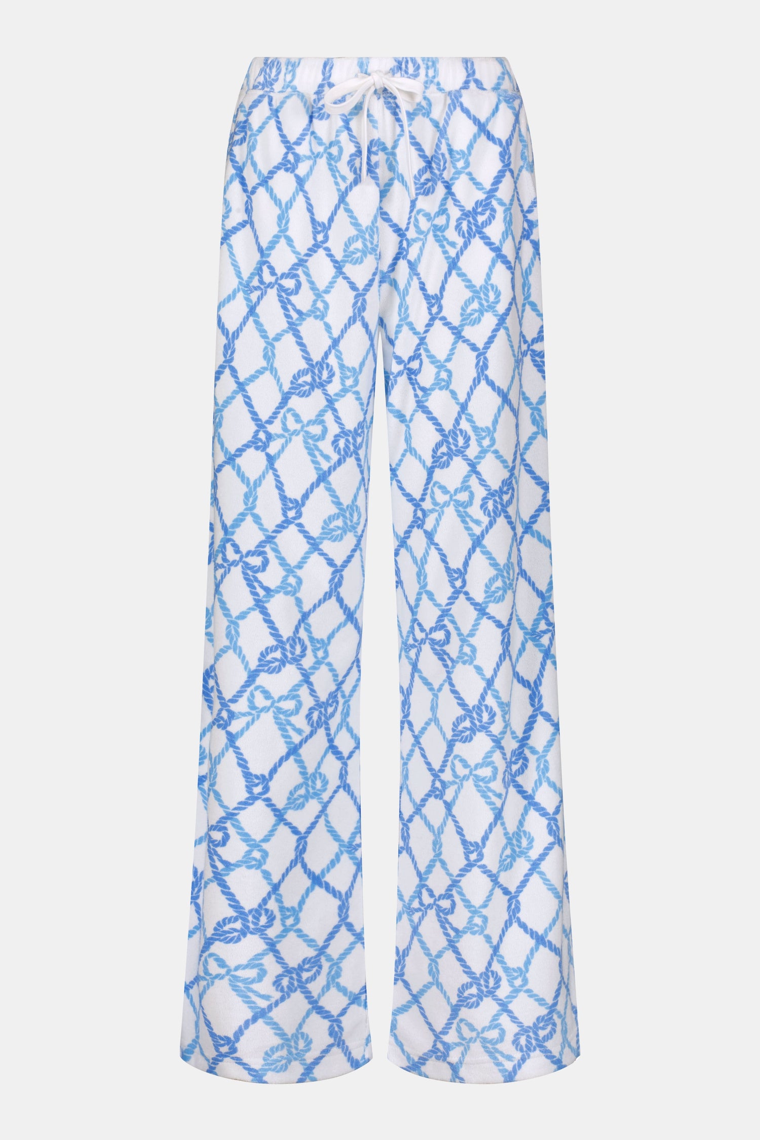 A person wears the Roller Rabbit Seaside Knots Mara Pant, featuring a tie waist and wide legs in loose white fabric with a light blue geometric chain pattern, paired with a matching top and white sandals against a plain white background.