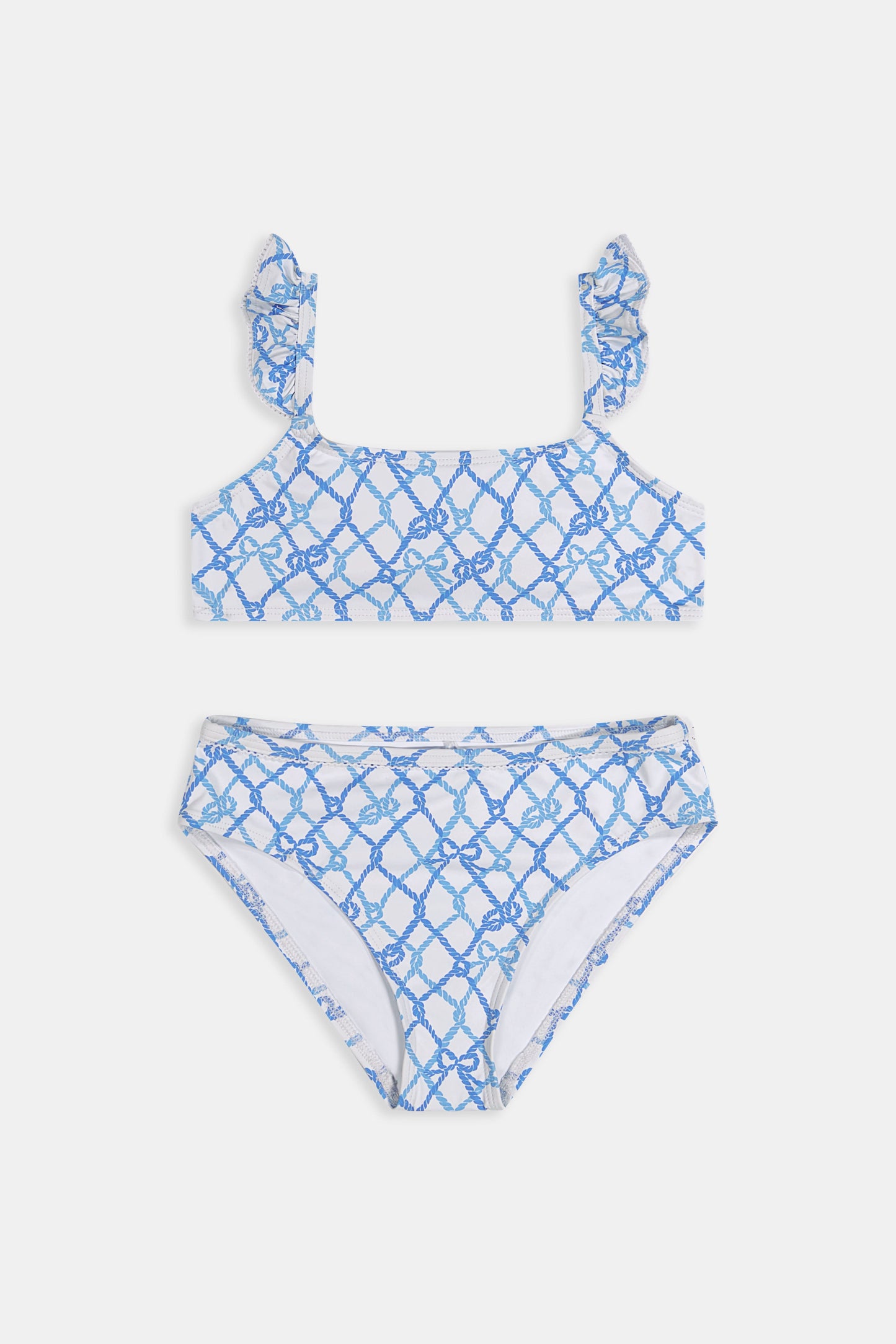 A young girl with curly hair smiles in the Roller Rabbit Kids Seaside Knots Rory Bikini, featuring ruffled shoulder straps and UPF 50+ sun protection, posing against a plain light background.