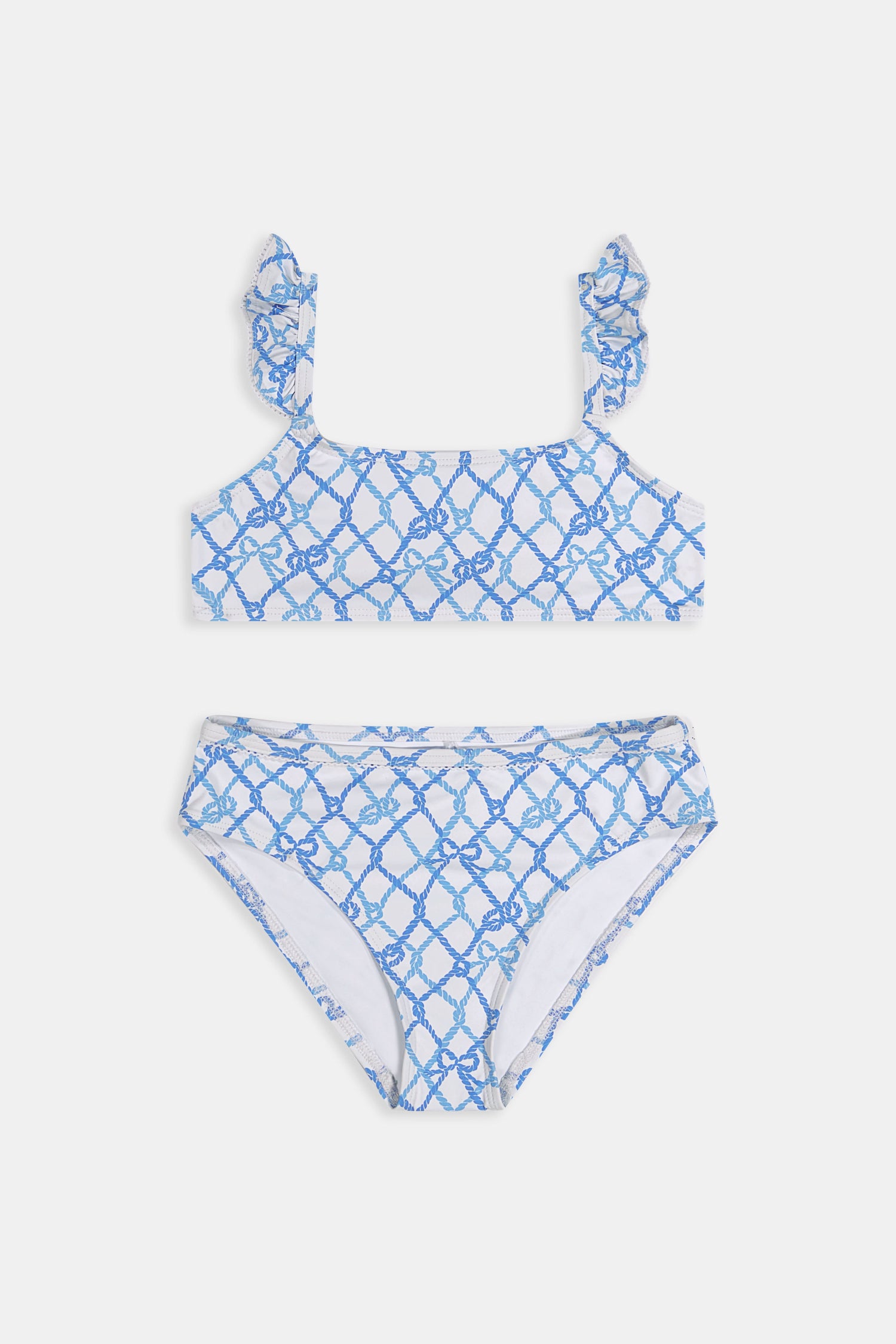 A young girl with curly hair smiles in the Roller Rabbit Kids Seaside Knots Rory Bikini, featuring ruffled shoulder straps and UPF 50+ sun protection, posing against a plain light background.