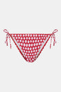 A person wears the Roller Rabbit Starry Dot Isa Bikini Bottom in red with white polka dots and adjustable hip ties, shown from mid-torso to upper thigh.