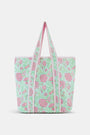 The Roller Rabbit Camellia Block Quilted Tote features pink and green floral patterns, a pale pink interior lining, and long white handles, shown on a plain white background.