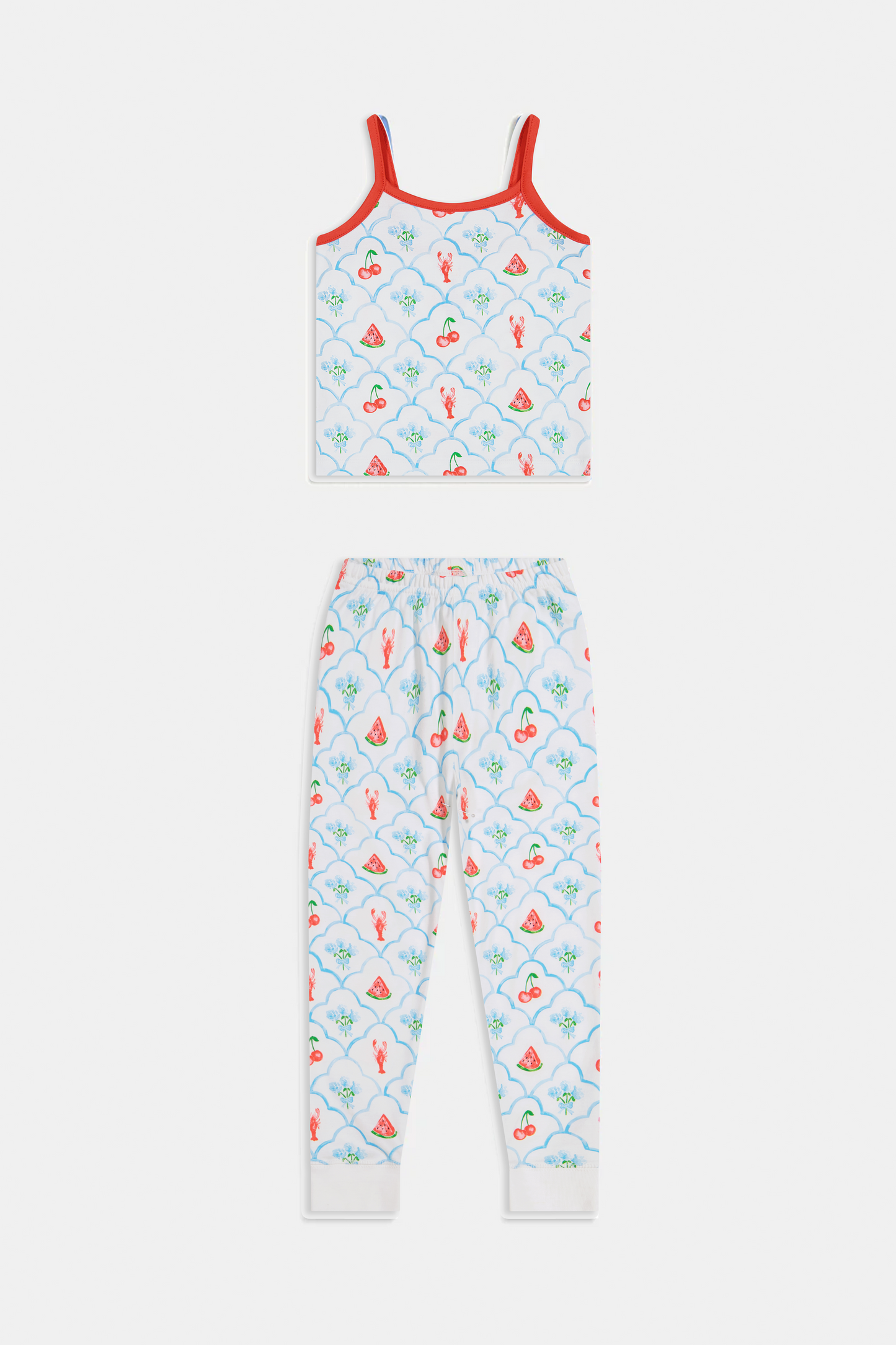 A young girl stands barefoot, smiling against a light background. She wears the Roller Rabbit Kids 4th of Jemina Noa Set—matching white Pima Cotton pajamas with red trim and a colorful flowers, butterflies, and birds print.