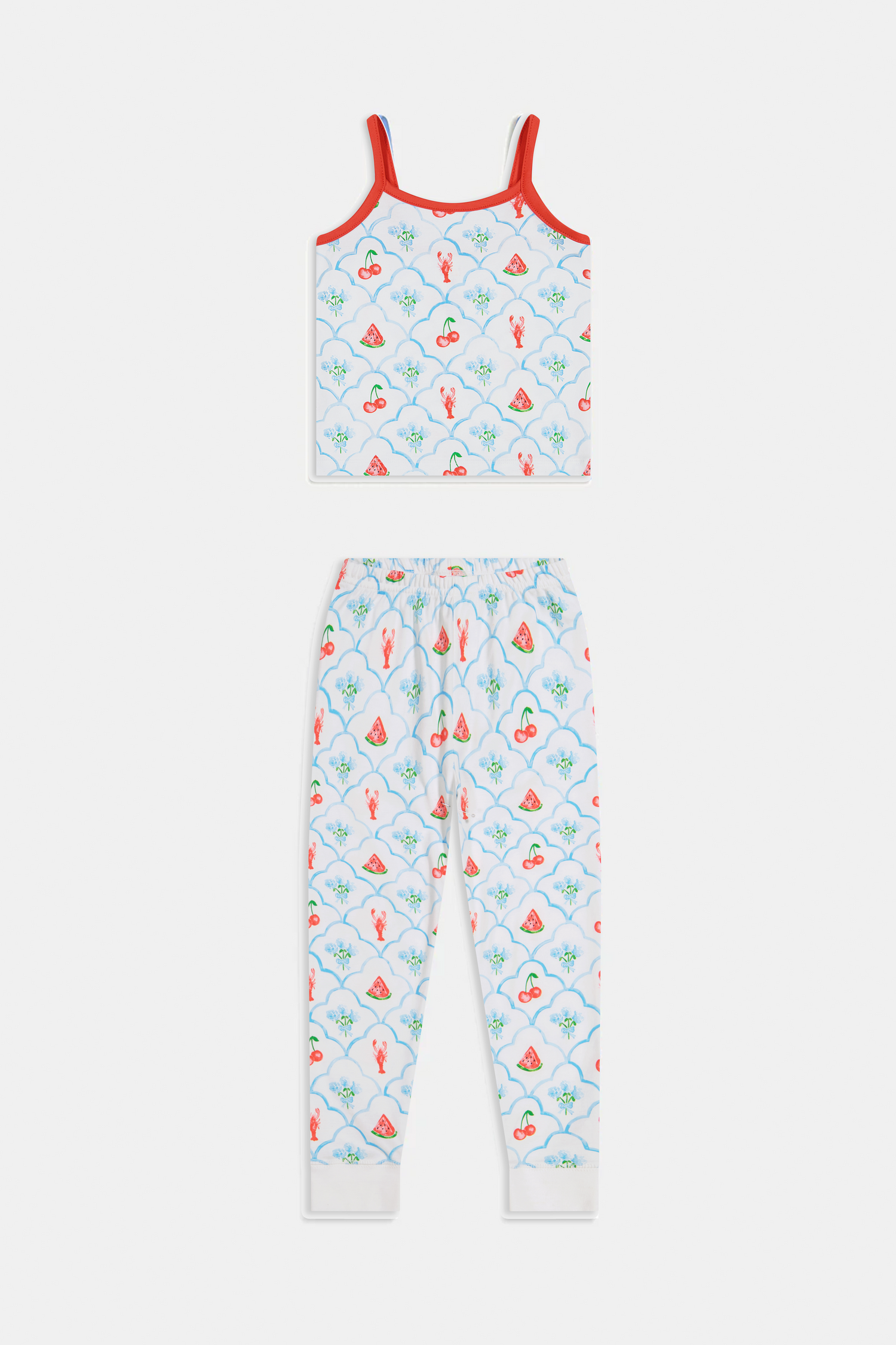 A young girl stands barefoot, smiling against a light background. She wears the Roller Rabbit Kids 4th of Jemina Noa Set—matching white Pima Cotton pajamas with red trim and a colorful flowers, butterflies, and birds print.