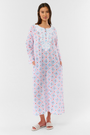 A woman with long hair wears the Roller Rabbit Lerato Inez Long Kurta, a cotton voile long sleeve pullover dress featuring a pastel pink and blue geometric pattern and white embroidery on the chest. She pairs it with white open-toe sandals.