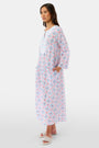 A woman with long hair wears the Roller Rabbit Lerato Inez Long Kurta, a cotton voile long sleeve pullover dress featuring a pastel pink and blue geometric pattern and white embroidery on the chest. She pairs it with white open-toe sandals.