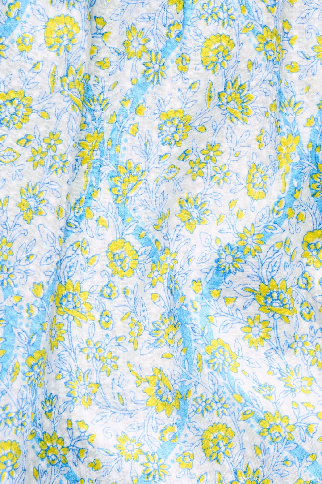Close-up of cotton seersucker fabric with yellow flowers and green leaves outlined in blue on white—light, crinkled texture ideal for floral ruffles on the Suzie Floral Ribbon Riki Skirt by Roller Rabbit.