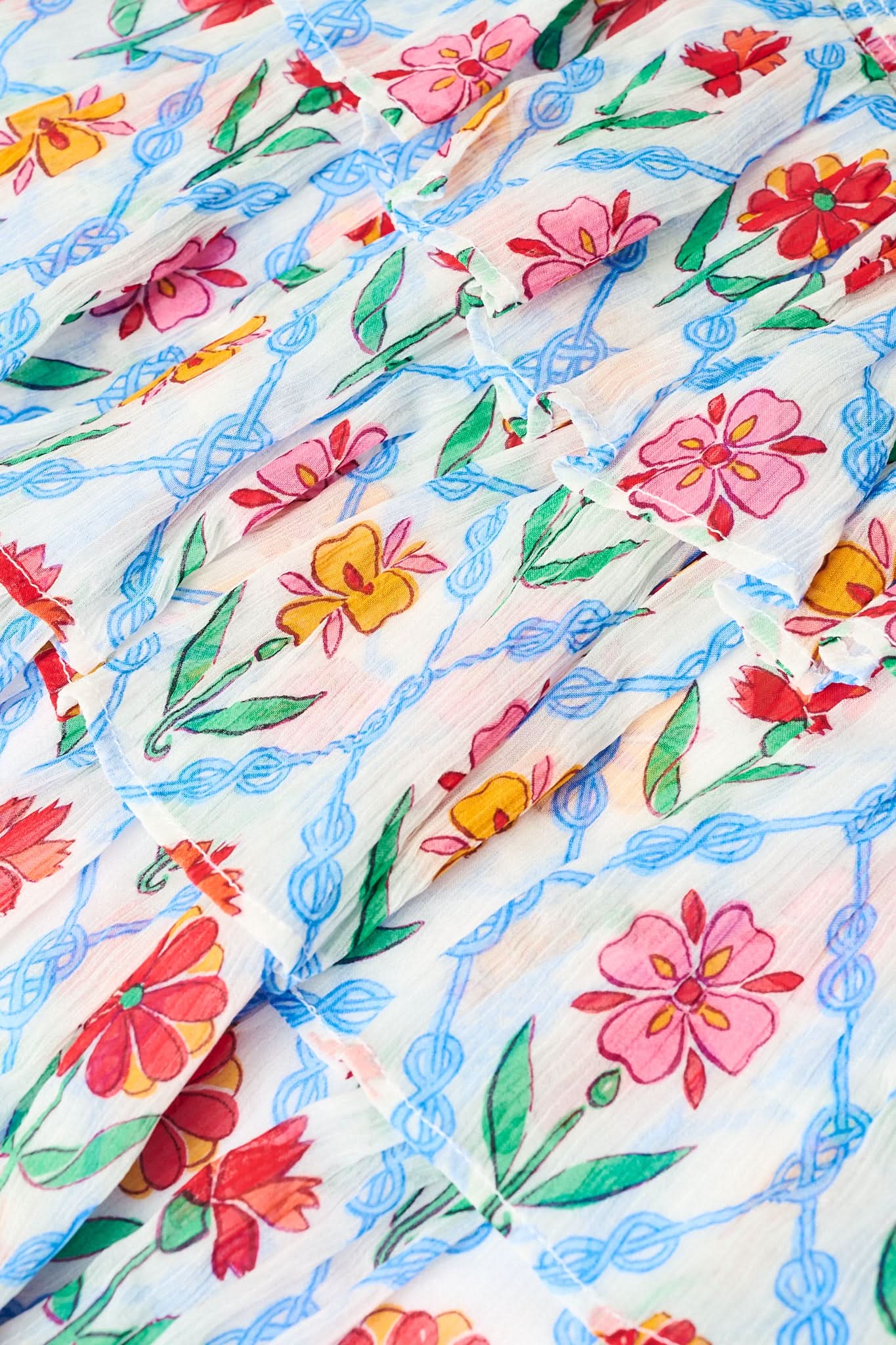 A close-up of the Roller Rabbit Infinity Floral Siggy Skirt, a crinkle chiffon mini with ruffles, featuring red, yellow, pink, and green florals on white. The skirt is styled with a white top.