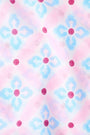 A woman with long hair wears the Roller Rabbit Lerato Inez Long Kurta, a cotton voile long sleeve pullover dress featuring a pastel pink and blue geometric pattern and white embroidery on the chest. She pairs it with white open-toe sandals.