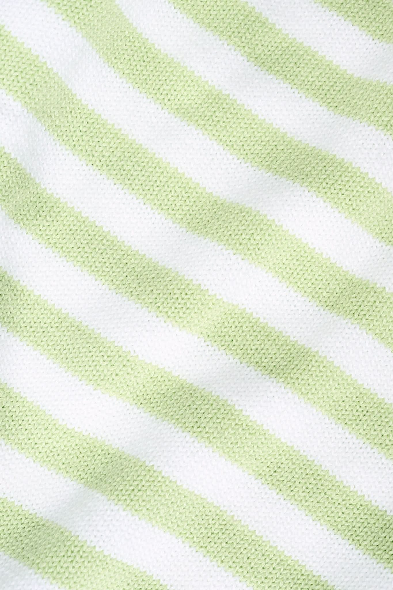 A woman with straight brown hair wears the Roller Rabbit Striped Hadley Sweater in sage green and white stripes, paired with white high-waisted pants and a beaded necklace, standing against a plain background and looking at the camera.