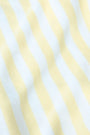 A young woman with light skin and long brown hair wears the Roller Rabbit Striped Rocio Sweater, a pastel yellow, lightweight cotton knit with a wide V-neck and collar. She pairs it with matching drawstring pants and gazes slightly to the side.