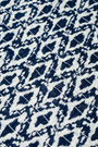A woman with long straight hair and a neutral expression wears the Roller Rabbit Diamond Ikat Isla Dress—a navy smocked sleeveless dress with a white ikat pattern, flared skirt, and dropped waist, standing against a plain background.