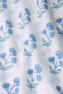 A young girl with long brown hair wears the Roller Rabbit Kids Rosa Ditsy Floral Pami Dress, made from cotton voile with blue-green block print and ruffled sleeves, standing against a plain light background, looking slightly to the side.